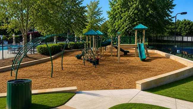 Children's playground with slides, climbing structures, green trees, and a pathway in a sunny park setting.