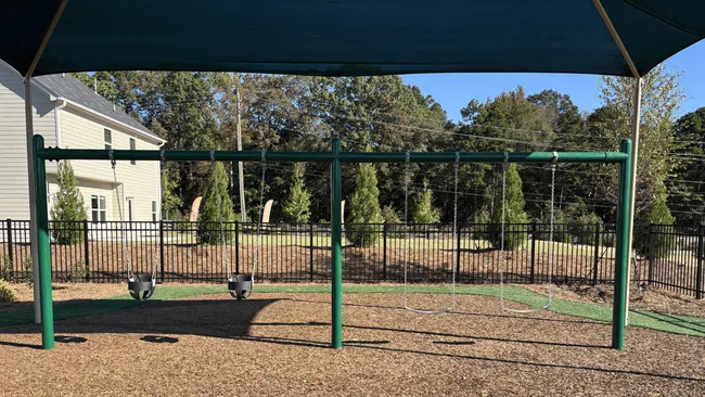 Empty swing set with toddler and regular swings under a shade structure in a sunny playground.