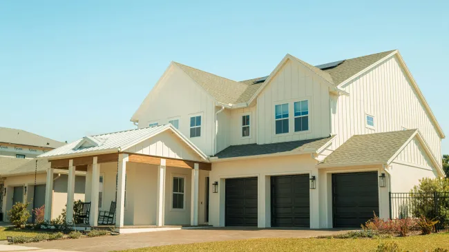 Modern two-story white house with three black garage doors and a covered porch with rocking chairs.