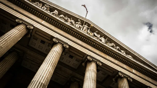Low angle view of classical courthouse with tall columns and sculpted figures under cloudy sky.