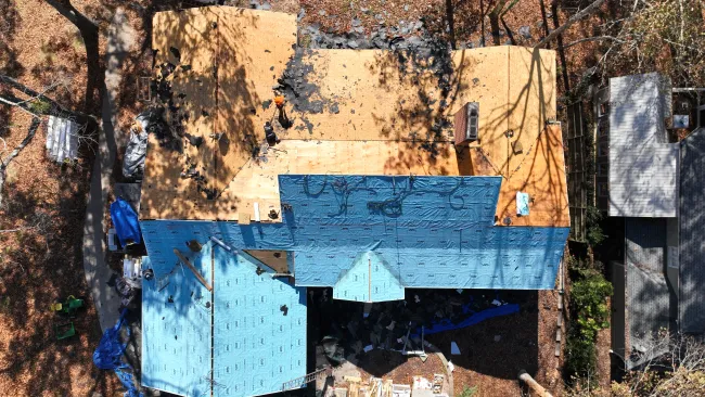 Aerial view of a house undergoing roof replacement with new blue underlayment installed on the partially stripped roof.