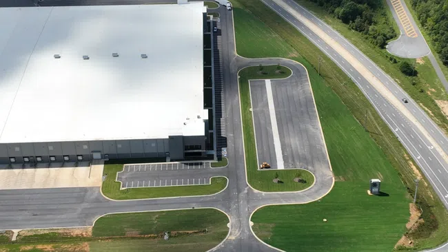 a large building with a large circular roof and a road with grass and trees