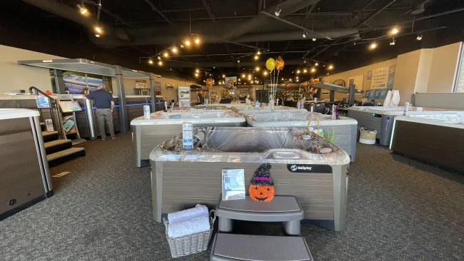 Showroom filled with various hot tubs on display, featuring warm lighting and festive decorations.