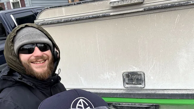 Two men smiling outdoors in winter clothing with a green and white Nissan truck in the background.