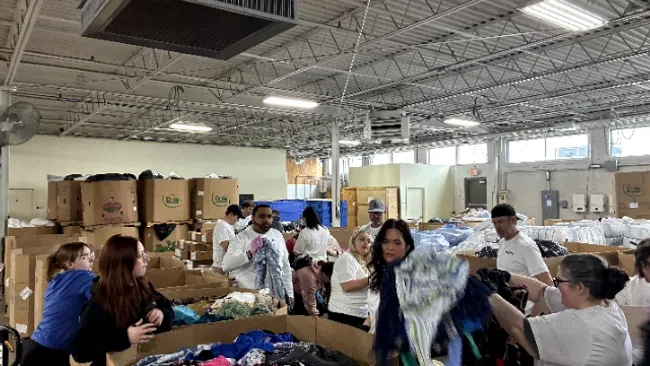 People sorting and organizing clothes in large bins inside a warehouse with high ceilings and industrial lighting.
