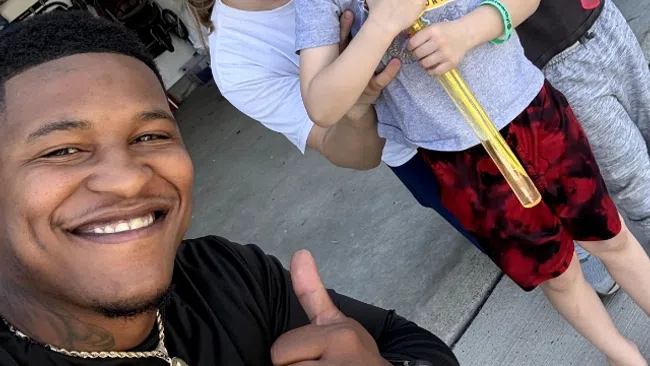 Smiling family posing in garage with two boys holding bubble wands and man giving thumbs up in selfie.
