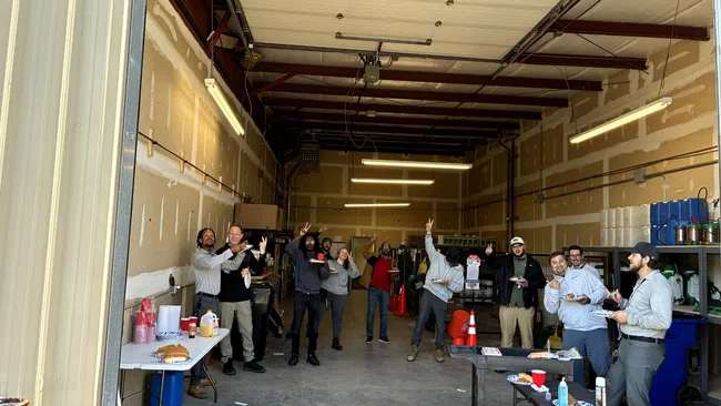 Group of coworkers having a casual gathering in a warehouse with food and drinks on tables.