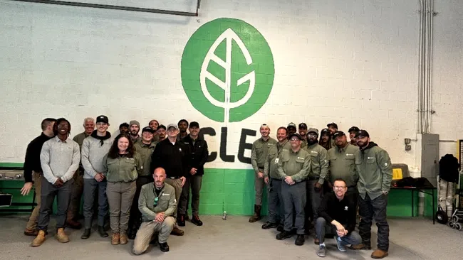Group photo of diverse team in green uniforms standing in front of a wall with a large green leaf logo.