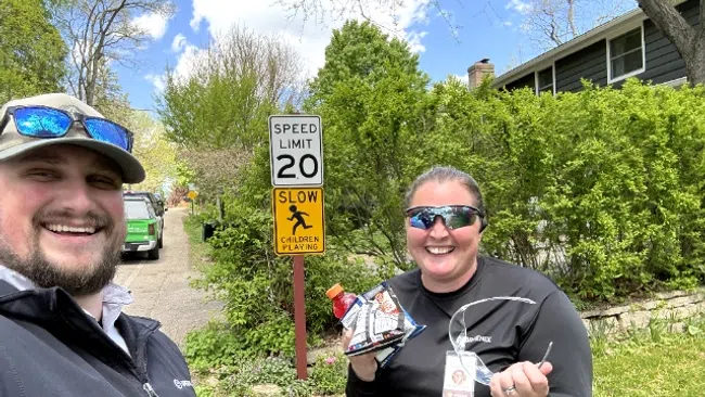 Two smiling adults outdoors near a speed limit and children playing sign on a sunny day with greenery