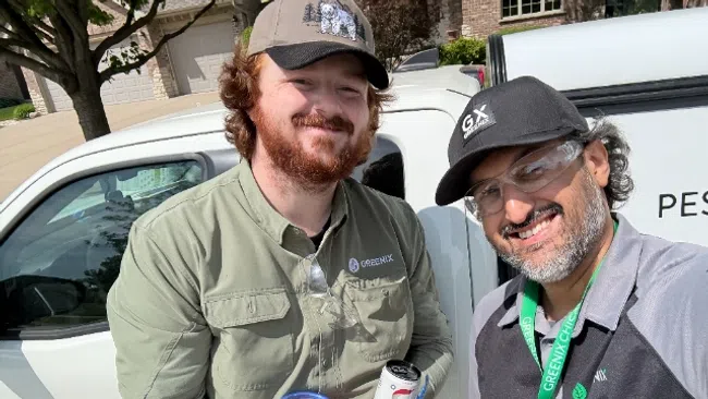 Two pest control workers smiling in front of a Greenix branded vehicle, holding a snack and a drink.