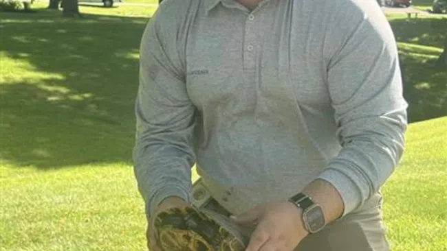 Man wearing sunglasses and cap, holding a baseball glove, ready to catch in sunlit park grass area.