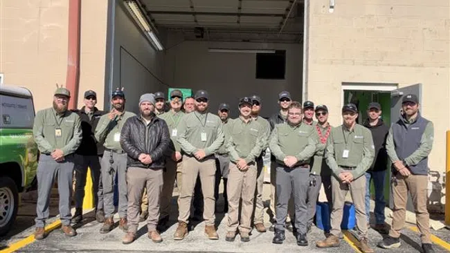 Group of employees in green uniforms posing outside a warehouse on a sunny day