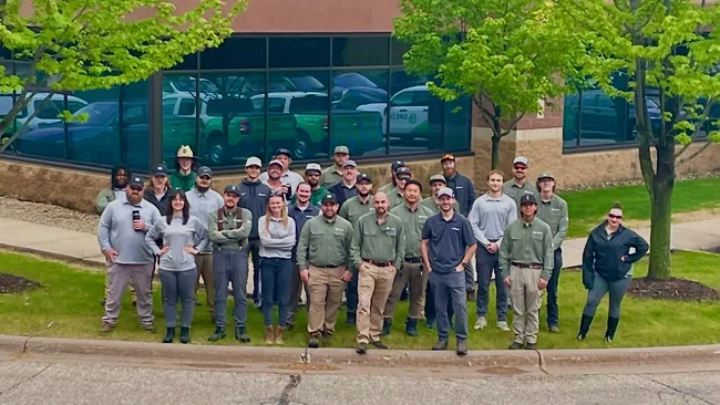 Group of diverse workers standing outside an office building on a grassy area near the street curb