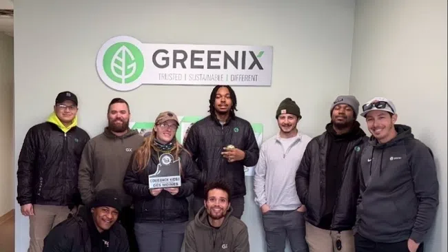 Group of nine people posing in front of a Greenix company sign inside an office space.