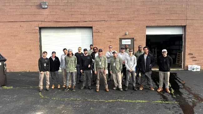 Group of workers standing outside a brown brick warehouse with two garage doors on a sunny day