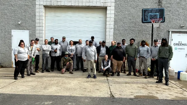 Group of employees posing outside a building with Grey and green uniforms near a basketball hoop.