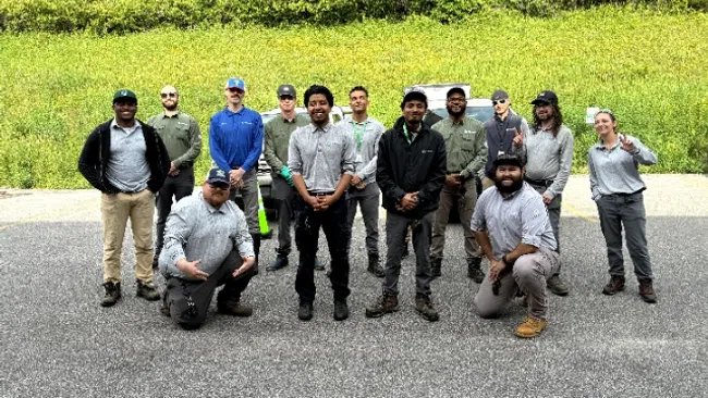 Group of twelve people outdoors on pavement with green bushes in the background, some kneeling and some standing.