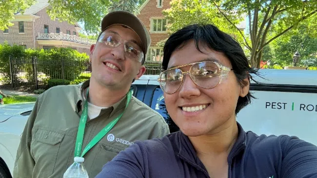 Two smiling Greenix Chicago pest control workers taking a selfie outdoors in front of a company van.