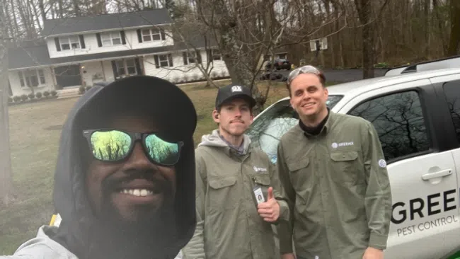 Three pest control workers smiling in front of a white Green Pest Control company vehicle outside a residential home.
