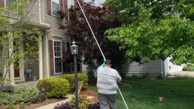 Person using a long pole with an orange ball to reach the roof of a suburban house on a sunny day.