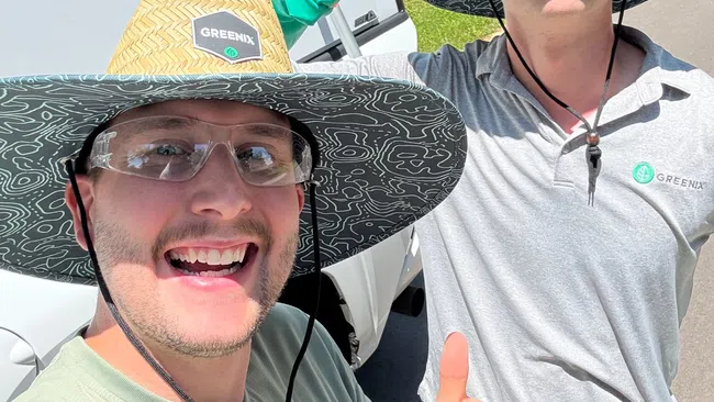 Two workers in Greenix hats and safety glasses giving thumbs up outside on a sunny day near a trailer.