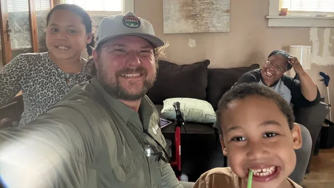 Smiling family taking a selfie in a cozy living room with couch, pillows, and wall art in the background