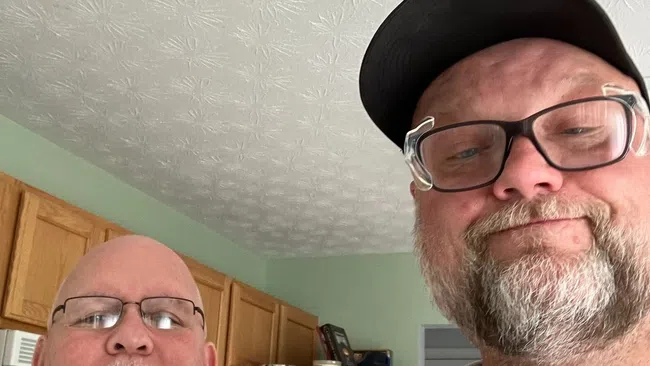 Two men with glasses smiling indoors, one holding a completed home inspection checklist in a kitchen setting.