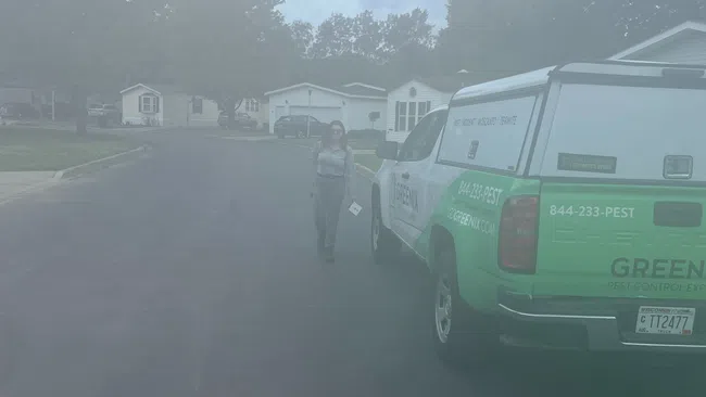 Technician walking toward a green pest control service truck in a suburban neighborhood on an overcast day