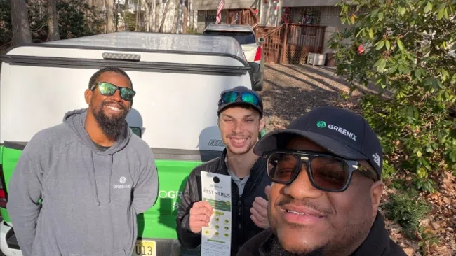 Three men in Greenix uniforms standing outside near a company truck in a residential area on a sunny day.