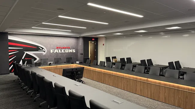 Modern conference room with long tables, black chairs, large TV monitors, and Atlanta Falcons branding on the wall.
