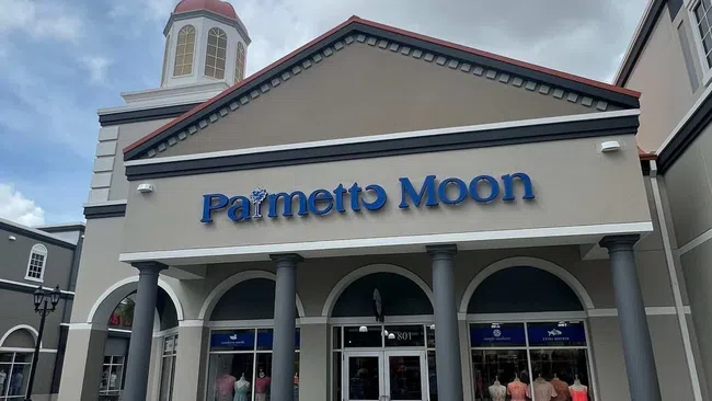 Exterior view of Palmetto Moon store with mannequins in the window and large columns under a cloudy sky.