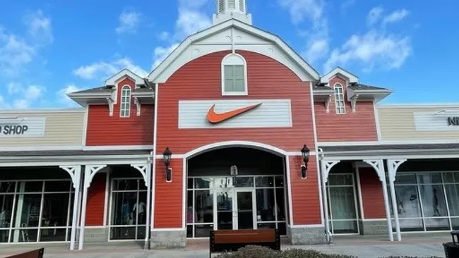 Exterior of a red and beige Nike store with a large orange swoosh logo under a blue sky