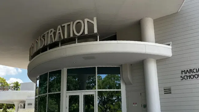 Modern curved entrance of Marcia School administration building with large windows and reflective glass doors.
