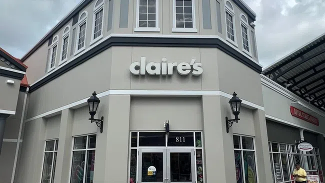 Claire's retail store exterior with large windows and a sign above the entrance under a cloudy sky.