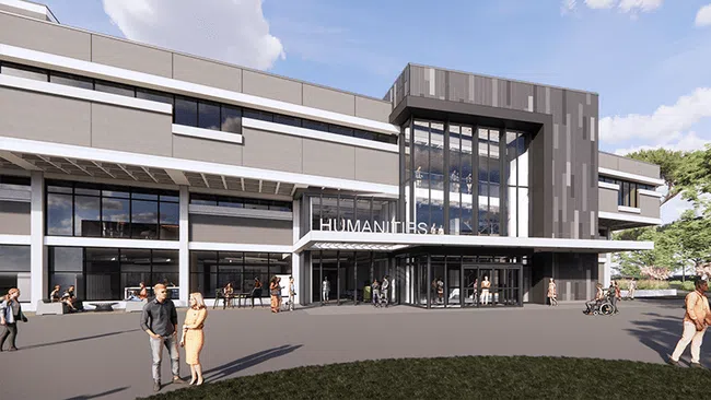Modern university humanities building with glass entrances and people walking outside on a sunny day