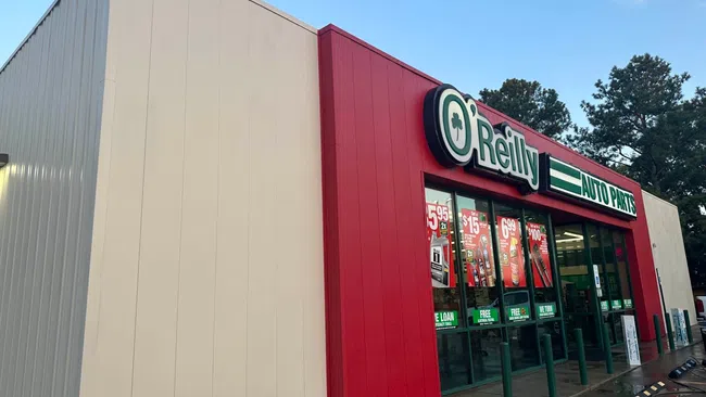 Exterior view of O'Reilly Auto Parts store with red and white facade and promotional posters on windows.