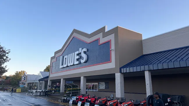 Exterior of Lowe's home improvement store with riding lawn mowers displayed outside on a clear day.