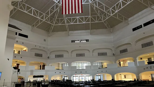 Spacious multi-level atrium with high ceiling, large American flag, and rows of tables and chairs below.