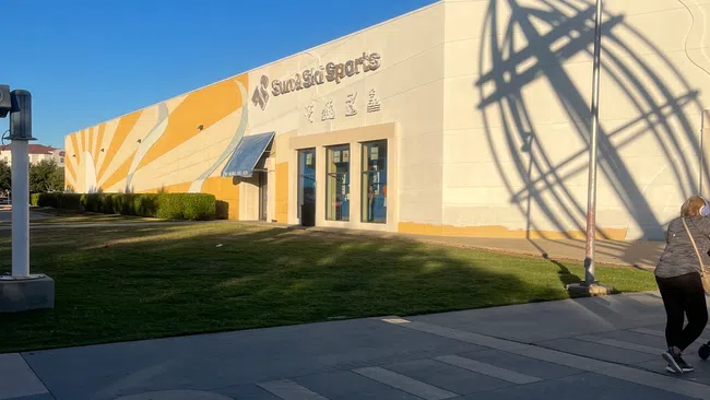 Sun & Ski Sports store with large yellow and white mural under clear blue sky and person walking nearby