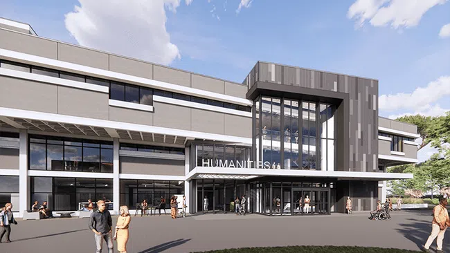 Modern Humanities building with large glass entrance, people walking and chatting outside on a sunny day.