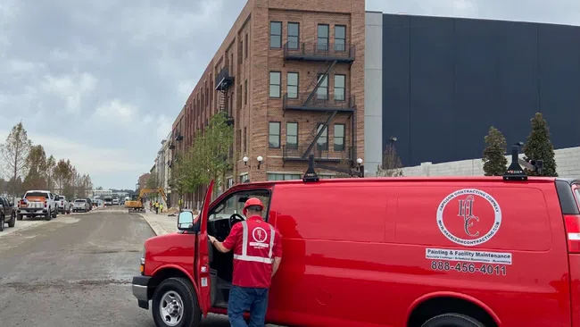 Worker in red uniform entering a bright red contractor van parked on a city street with buildings and construction in background