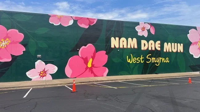 Mural of pink flowers and text Nam Dae Mun West Smyrna on green wall beside empty parking lot