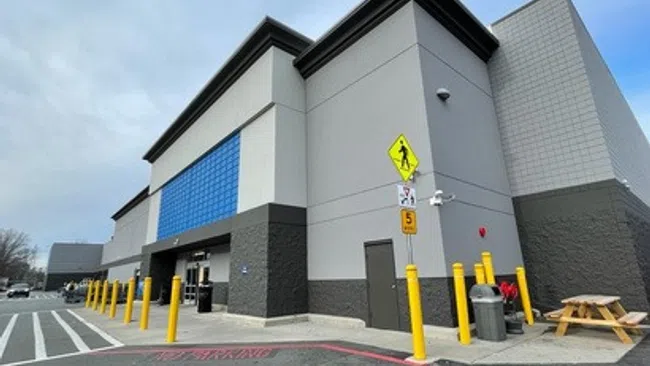 Modern commercial building with gray and blue exterior, yellow safety poles, and pedestrian crossing signs in parking lot.