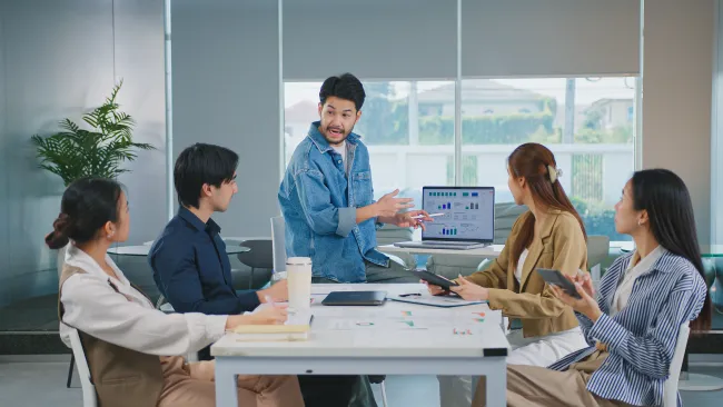 Team meeting with diverse young professionals discussing data charts on a laptop in a modern office.