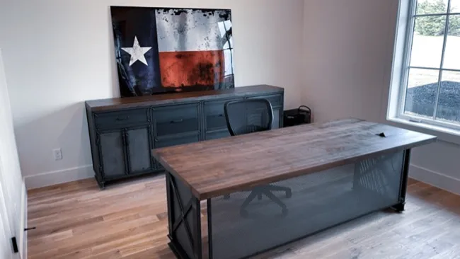 Industrial-style office with wooden desk, black metal cabinet, mesh chair, and Texas flag artwork on wall