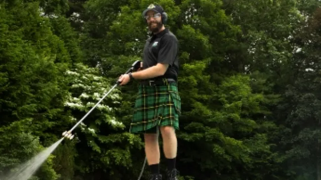 a man wearing a kilt and pressure washing