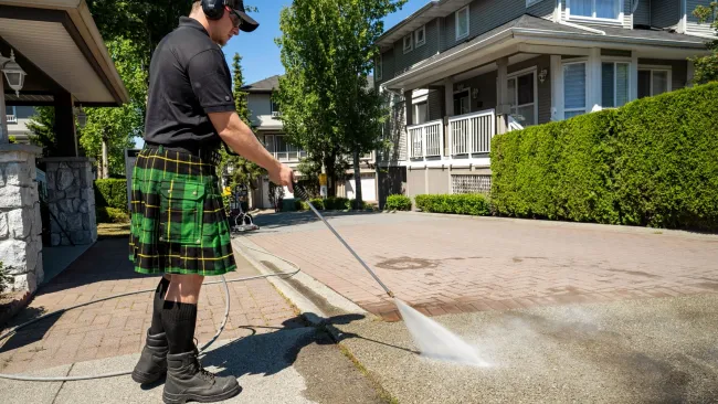 a man wearing a kilt and washing off a driveway