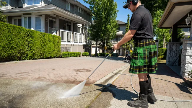 a man wearing a kilt pressure washing a sidewalk