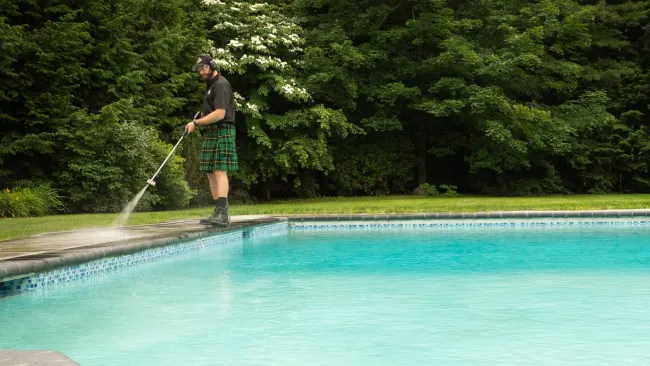 a man pressure washing beside a pool