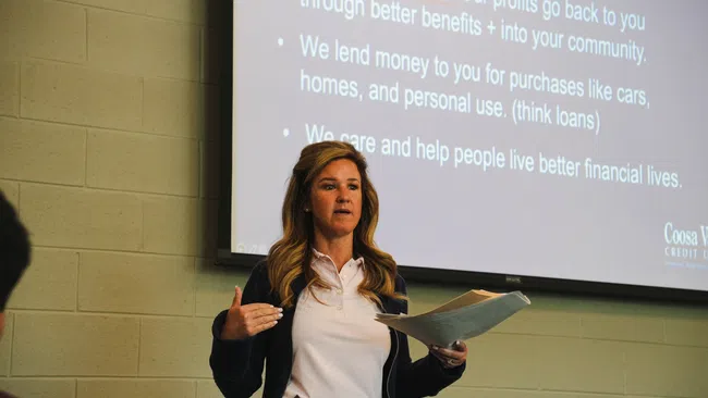 Woman giving a presentation on financial services with projected text on loans and community benefits